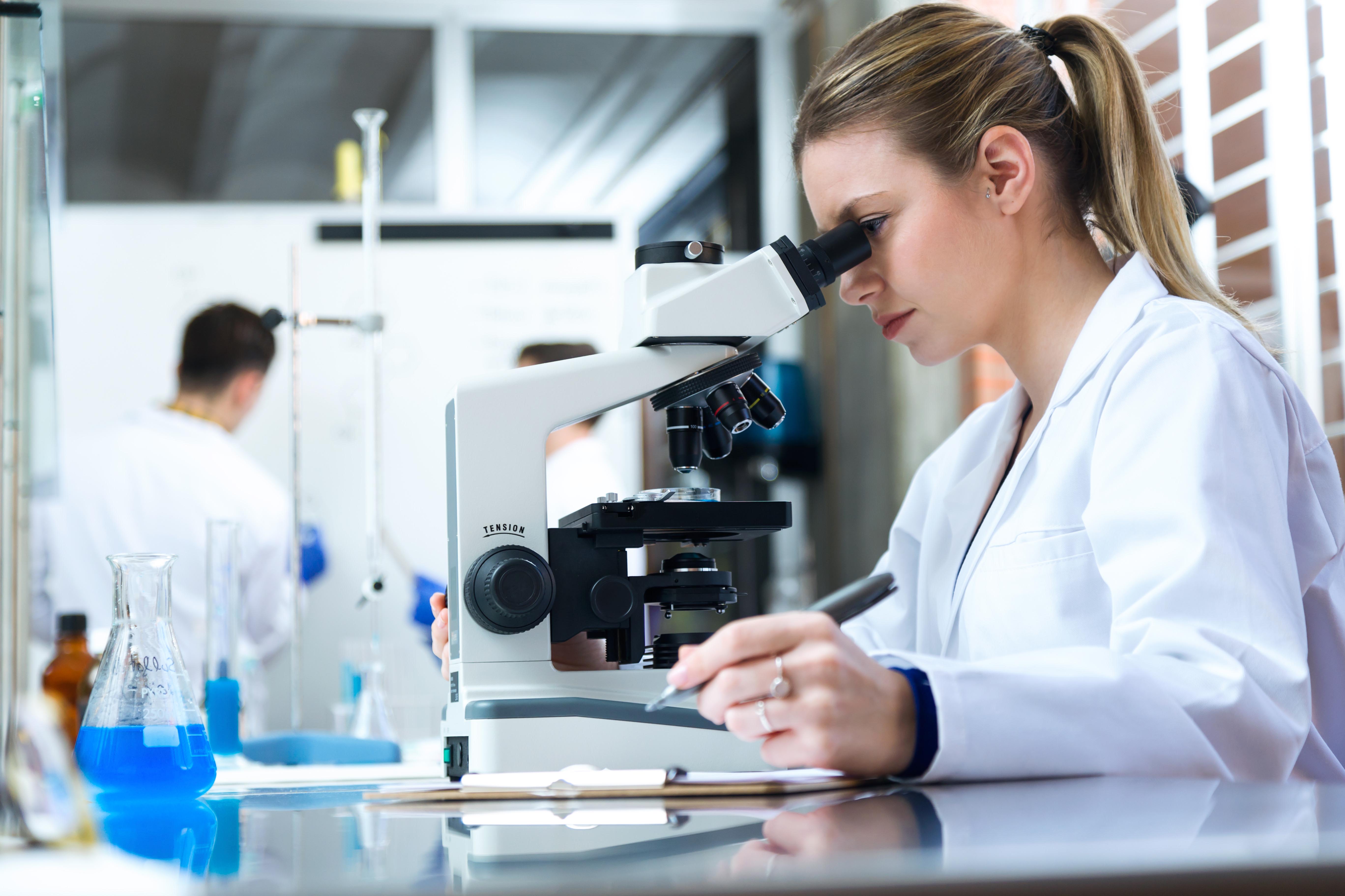 Portrait of young woman looking through microscope in laboratory.